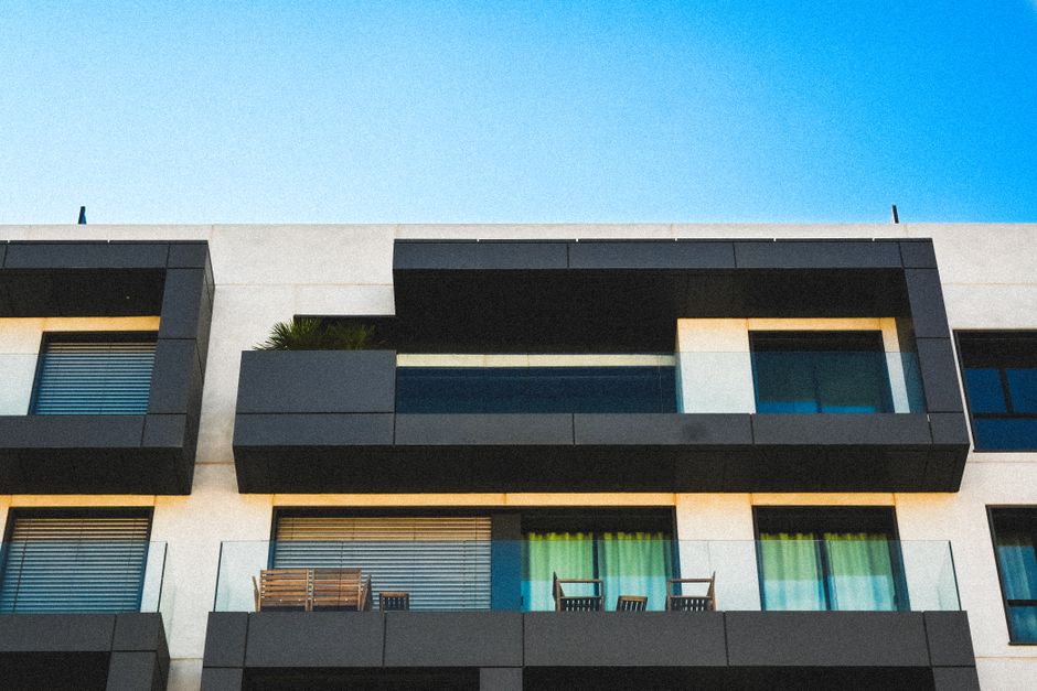 Minimalist apartment facade with glass balconies against a clear blue sky