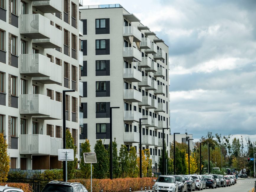 Contemporary apartment complex on a city street lined with parked cars and autumn foliage